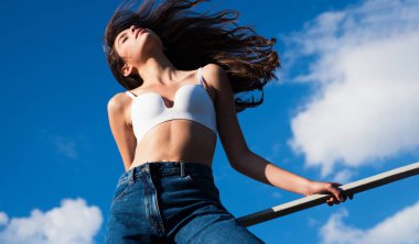 Denim modası. Gökyüzü arka planında kot pantolonlu seksi kız. Kadın pantolonu. Moda sezonu. Sıradan moda.