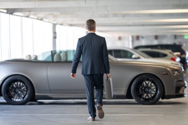 Lüks arabanın yanında başarılı bir iş adamı. Başarılı iş adamı. Şık ceketli, olgun, başarılı bir iş adamı. Takım elbiseli zengin iş adamı dışarıda yürüyor. Lüks başarılı iş adamı. İş başarısı