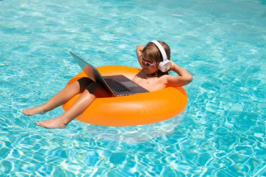 Yaz işleri ve online teknoloji. Yazın havuz başında dizüstü bilgisayarı olan bir çocuk. Su geçirmez laptop