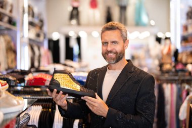 Erkek için spor ayakkabısı. Moda ayakkabıları. Ayakkabı mağazasında şık bir adam. Ayakkabı seçen olgun bir adam. Yapay elmaslar koleksiyonu olan bir spor ayakkabı tasarımcısı. Lüks mağazada zengin stil ve cazibeli adam