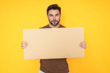 Stüdyo arka planında boş afiş olan bir adam. Elinde boş poster tutan çekici bir adamın portresi. Boş poster gösteren bir adam. İşaret panosu, pano ya da pano ile kopyalama alanı sunuluyor
