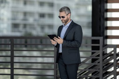 Finans uzmanı bir kontratı inceliyor. Tabletli bir iş adamı. Dışarıda tablet kullanan bir iş adamı. Olgun iş adamı finans verilerini kontrol ediyor. Tabletteki zengin işadamı gözden geçirme sözleşmesi