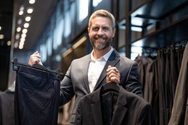 Takım elbiseli, butikte şık bir adam. Bir iş adamı mağazada şık bir takım elbise seçer. Modayı takip eden bir müşteri resmi kıyafet alırken ceketi inceler. Klasik kıyafetli çekici bir manken.