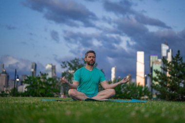 Nilüfer çiçeğinin içinde meditasyon yapan olgun bir adam. Sporcu şehir parkında yoga yaparken asana meditasyonu yapıyor. Atletik erkek meditasyonu, rahatlama, sağlıklı yaşam tarzı kavramı. Açık havada meditasyon.