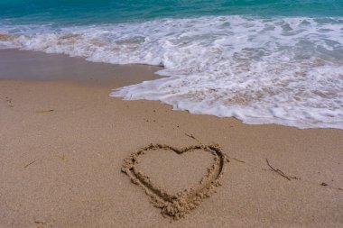 Deniz kumsalı. Manzaralı deniz sahili arkaplanı. Cennet okyanus manzarası. Kalp kumda çizilmiş. Dalgalar kalp şeklinde bir işaret oluşturuyor. Kumsalda aşk. Romantik yaz. Kumdan yapılmış bir kalp. Aşk ve okyanus dalgaları