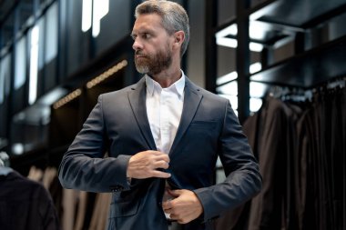 Takım elbiseli, takım elbiseli bir adam. Bir iş adamı mağazada şık bir takım elbise seçer. Modayı takip eden bir müşteri resmi kıyafet alırken ceketi inceler. Klasik kıyafetli çekici bir manken.