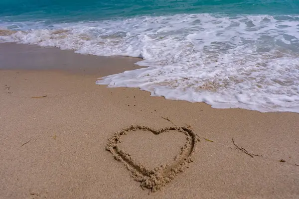 Deniz kumsalı. Manzaralı deniz sahili arkaplanı. Cennet okyanus manzarası. Kalp kumda çizilmiş. Dalgalar kalp şeklinde bir işaret oluşturuyor. Kumsalda aşk. Romantik yaz. Kumdan yapılmış bir kalp. Aşk ve okyanus dalgaları