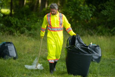 Lastik eldivenli gönüllü, çöp torbasıyla dışarıdaki ormandaki çöpleri temizliyor. Eko, çevre koruma. Kirliliği geri dönüştür. Çöpleri ve plastik çöpleri toplayan adam. Ortamı kaydet