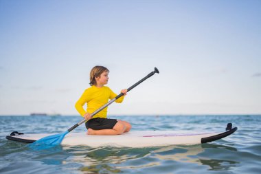 Çocuk ayakta yüzme tahtasında yüzüyor. Su sporları, aktif yaşam tarzı. Okyanusta kürek çeken bir çocuk var. Çocuk Paddle binicisi. Yaz Suyu sporu, SUP sörfü. Yaz tatili