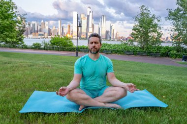 Hispanik Adam dışarıda otların içinde meditasyon yapıyor. Sporcu şehir parkında yoga yaparken asana meditasyonu yapıyor. Atletik erkek meditasyonu, rahatlama, sağlıklı yaşam tarzı kavramı. Açık havada meditasyon.