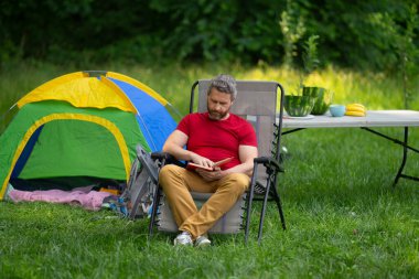 Gezgin doğada kamp yapmaktan hoşlanıyor. Doğaya yaz gezisi. Orman kampında dinlenen adam. Kamp gezisi. Yürüyüşten sonra çadırın yanında dinleniyor. Barışçıl bir kamp alanında özgürlük tatili. Yazın piknikteki adam