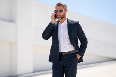 Ofis çalışanı dışarıda cep telefonuyla konuşuyor. Girişimci cep telefonundan konuşur. Yönetici telefon görüşmesi yapıyor. Telefon kullanan şık bir iş adamı. İş görüşmesi. Meşgul iş adamı telefonda konuşuyor.