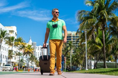 Miami 'nin güneşli sokaklarında bir turist yürüyor. Bir erkek turist, tropikal bir şehirde yaz tatilinin tadını çıkarır. Bavullu bir turist şehir manzarasını keşfediyor. Erkek turist şehirde yürüyor