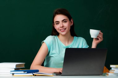 Öğrenci sınıfta kahve içiyor. Üniversitede kahve molası. Öğrenci kız kahve fincanı tutuyor. Üniversite öğrencisi tahtanın yanında öğreniyor. Eğitim konsepti. Üniversitede ders ve ödev