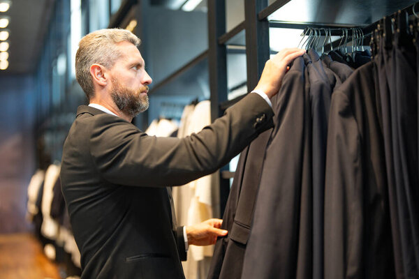 Классический костюм. Латиноамериканский бизнесмен ценит хороший пошив и костюм. Хорошо одетый мужчина позирует в бутике костюмов. Помощник продавца помогает стильному человеку найти идеальный костюм