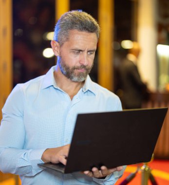 Gece lambasında dizüstü bilgisayar kullanan bir iş adamı. İşadamı sokakta dizüstü bilgisayarda çalışıyor. Orta yaşlı iş adamı gece kulübü yakınlarında iş planlıyor. 40 'lı yaşlarda bir iş adamı. Serbest Çalışan açık havada dizüstü bilgisayarda geziniyor