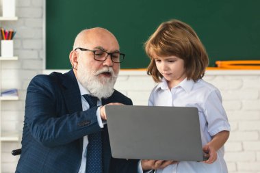 Kıdemli öğretmen ve okul çocuğu. Olgun öğretmen, okul çocuklarının öğrenmesine yardımcı olur. Okul öğretmeni ve çocuk sınıfta. Okulda ders veren öğretmen çocuğa dizüstü bilgisayarda öğretiyor.