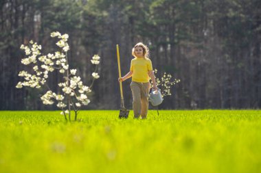 Bahçede çalışan bir çocuk. Çevre için büyüyen ağaç ve bakım bitkisi. Ekim mevsimi. Bitki yetiştiren bir çocuk. Bahçe işleri. Meyve sulayan çocuk. Çocuk dikme ağacı. Bahar günü