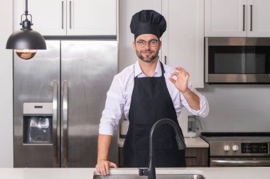 Chef cook with ok sign, delicious food. Portrait of chef man in a chef cap in the kitchen. Man wearing apron and chefs uniform and chefs hat. Character kitchener, chef for advertising