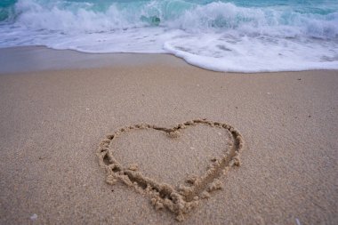 Kalp kumda çizilmiş. Dalgalar kalp şeklinde bir işaret oluşturuyor. Kumsalda aşk. Romantik yaz. Kumdan yapılmış bir kalp. Aşk ve okyanus dalgaları