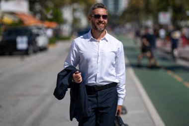 İş adamı işe yürüyerek gider. Hispanik iş adamı sokakta güven içinde yürüyor. Ofis çalışanı ofise gidiyor. Olgun bir iş adamı şehirde yürüyor. Dışarıda dolaşan gömlekli bir iş adamı.