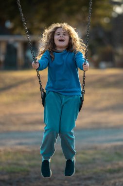 Salıncaktaki çocuk. Çocuk bahçesinde mutlu bir çocuk. Kaygısız çocuk dışarıda sallanıyor. Mutlu çocuklar dışarıda oynuyor. Sarışın çocuk mutluluktan uçuyor. Dışarıdaki oyuncu çocuk. Çocuk suratı. Mutlulukla sallanan çocuk