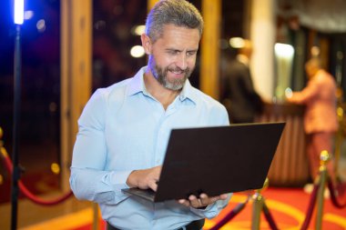 Gece sokakta dizüstü bilgisayar kullanan bir iş adamı. İş adamı dışarıda dizüstü bilgisayarda çalışmayı planlıyor. İşadamı, neon şehir ışıkları altında dizüstü bilgisayarda geziniyor. Serbest çalışan bir iş adamı. Gece işi.