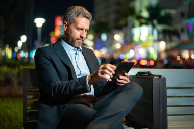 Dışarıda tablet üzerinde çalışan bir iş adamı. Tabletli bir iş adamı. Gece sokağında tabletli bir iş adamı. Tablet kullanan bir işadamı, bankta oturur. Gece işi.