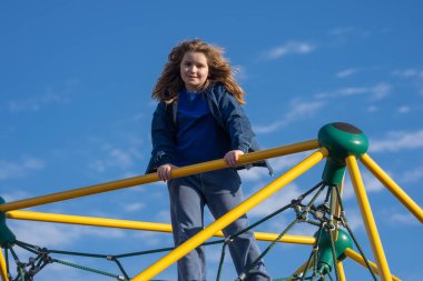 Tırmanışta oynayan çocuk. Oyun parkına tırmanan aktif bir çocuk. Çocuk parka tırmanıyor. Mutlu çocuk dışarıda oynamaktan hoşlanıyor. Sevimli çocuk oyun alanında eğleniyor. Çocuk parka tırmanıyor