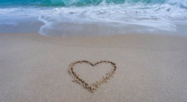 Kalp kumda çizilmiş. Dalgalar kalp şeklinde bir işaret oluşturuyor. Kumsalda aşk. Romantik yaz. Kumdan yapılmış bir kalp. Aşk ve okyanus dalgaları