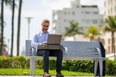 Açık havada dizüstü bilgisayar üzerinde çalışan başarılı bir iş adamı. Kendine güvenen bir iş adamı elinde dizüstü bilgisayarla bankta oturuyor. İspanyol iş adamı uzaktan çalışıyor. Zengin iş adamı yazın internette çalışıyor.