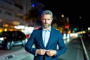 Gece vakti poz veren başarılı bir iş adamı. Gece sokağında takım elbiseli zengin bir adam duruyor. Resmi takım elbiseli yakışıklı bir iş adamı. Şık bir iş adamı. Zarif bir iş adamı. Zengin iş adamı.