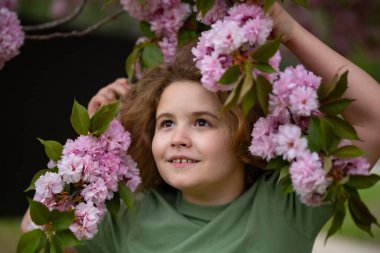 Çocuğun etrafında bahar çiçekleri var. Çiçek açan bahçede bir çocuk. Çiçeklere yakın bir çocuk yüzü. Hayalperest çocuk portresi. Açık havada çocuklar çiçek açan ağaçlarla portre yaparlar. Çocuğa ve çiçeklere yakın çekim