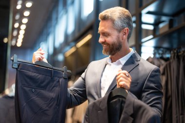 Bir adam butikte alışveriş yaparken klasik bir terzi kıyafeti giyer. Başarılı bir iş adamı için klasik bir kıyafet. Takım elbiseli modaya uygun bir mağaza. Olgun bir adam bir takım elbise seçer. Bir erkek resmi etkinlik için takım elbise seçer.