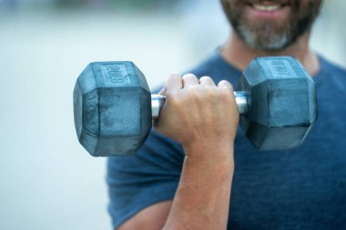 Dambıllar kol kola. Yetişkin bir adamın dambılları dışarı kaldırması. Kol kasları dambıl egzersizi yapıyor. Kol halteri tutun. Dambılı bir erkek kolunun yakın çekimi.