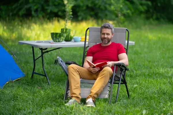 Adam doğada kamp yapmayı seviyor. Doğaya yaz gezisi. Orman kampında dinlenen bir turist. Kamp gezisi. Yürüyüşten sonra çadırın yanında dinleniyor. Barışçıl bir kamp alanında özgürlük tatili. Yazın piknikteki adam