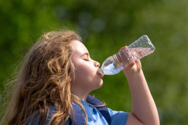 Şişeden su içen çocuk. Çocuk içkiyle ferahlatıyor. Susamış çocuk plastik şişeden su içiyor. Susamış çocukların yüzüne yakın çekim. Doğada taze su. Susamış çocuk için saf su şişesi.