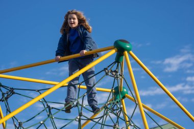 Çocuk dışarı tırmanıyor. Oyun parkına tırmanan aktif bir çocuk. Çocuk parka tırmanıyor. Mutlu çocuk dışarıda oynamaktan hoşlanıyor. Sevimli çocuk oyun alanında eğleniyor. Çocuk parka tırmanıyor