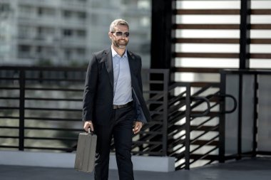 Başarılı bir iş adamı bir evrak çantasıyla dışarıda yürüyor. İş adamı hareket halinde. Takım elbiseli olgun bir avukat. Çantası olan zengin bir iş adamı. Orta yaşlı iş adamı işe gidiyor. Yakışıklı avukat.