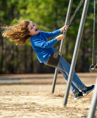 Heyecanlı çocuk eğleniyor. Çocuk bahçesinde mutlu bir çocuk. Havada sallanan tasasız çocuk. Mutlu çocuklar dışarıda oynuyor. Genç çocuk heyecanla sallanıyor. Dışarıdaki oyuncu çocuk. Komik çocuk yüzü.