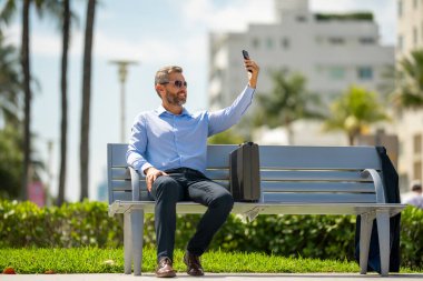 Açık havada dizüstü bilgisayar üzerinde çalışan başarılı bir iş adamı. Kendine güvenen bir iş adamı elinde dizüstü bilgisayarla bankta oturuyor. İspanyol iş adamı uzaktan çalışıyor. Zengin iş adamı yazın internette çalışıyor.