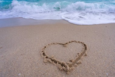 Kalp kumda çizilmiş. Dalgalar kalp şeklinde bir işaret oluşturuyor. Kumsalda aşk. Romantik yaz. Kumdan yapılmış bir kalp. Aşk ve okyanus dalgaları