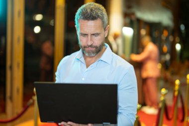 Gece sokakta dizüstü bilgisayar kullanan bir iş adamı. İş adamı dışarıda dizüstü bilgisayarda çalışmayı planlıyor. İşadamı, neon şehir ışıkları altında dizüstü bilgisayarda geziniyor. Serbest çalışan bir iş adamı. Gece işi.