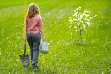 Çocuk bahar ağacı dikiyor. Çocuklar meyve ağacı gibi büyür. Kürekli çocuk bahçıvan. Çocuk meyve bahçesinde çiçek açan ağaçlarla çalışıyor. Çocuklar arka bahçeye ağaç dikiyorlar. Ağaçlarla ilgilenen genç çiftçi