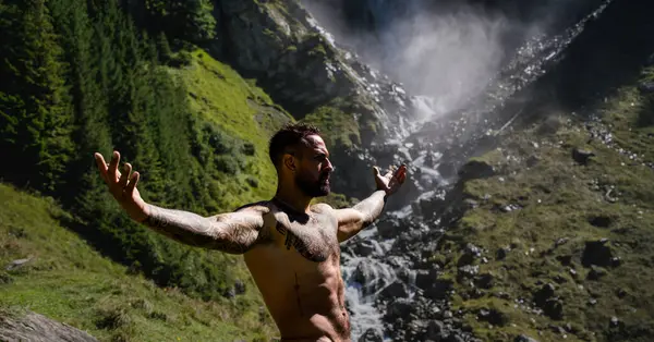 Tasasız ve özgür. Yaz tatilindeki erkek turist. Yaz tatilinde çıplak gövdeli yakışıklı bir adam. Dışarıda seksi bir yürüyüşçü var. Şelale manzarasında yürüyen bir turist. İnsan Seyahati ve doğa