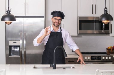 Tamam işareti olan bir aşçı, lezzetli yemekler. Mutlu fırıncı. Aşçı aşçı adam. Milenyum aşçı üniformalı erkek şef. Aşçı mutfakta yemek pişiriyor.