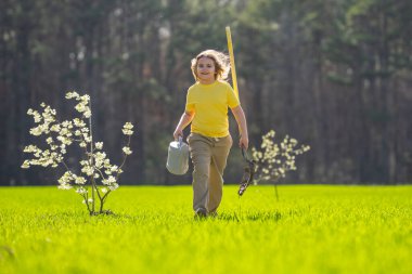 Ağaç diken bir çocuğun portresi. Çocuk bahçıvan. Bahçede çalışan bir çocuk. Çevre için büyüyen ağaç ve bakım bitkisi. Ekim mevsimi. Bitki yetiştiren bir çocuk. Bahçe işleri.