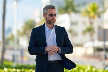 Olgun iş adamı şehirde güvenle yürüyor. Sokakta yürüyen bir iş adamı. Ofise doğru yürüyen yakışıklı bir iş adamı. Açık havada yürüyen kendinden emin bir girişimci.