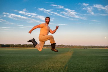 Bir çiftçi tarladan atlıyor. Çiftlik alanındaki eğlenceli çiftçi. Çiftçi tarlaya atladı. Mutlu tarım işçisi. Kırsal işçi atlayışı. Çiftçi çiftlikten atlıyor. İyi hasat