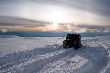 01.02.2021, Karpatlar. Gün batımında kar içinde off-road SUV. 4x4 jipli bir kış seferi. Kış doğasında zorlu bir off-road gezisi. Off-road arabalı dağ yolu. Kar yolunda macera gezisi